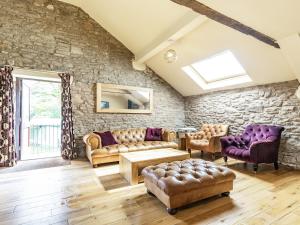 a living room with leather furniture and a stone wall at The Hayloft in Whaley Bridge