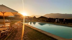 a swimming pool with chairs and an umbrella and the sunset at Gran Parcela Monte de Olmue in Olmué