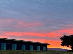 un bâtiment dans un champ avec un coucher de soleil en arrière-plan dans l'établissement “The Cliffs” Humpridge View Motels, à Tuatapere