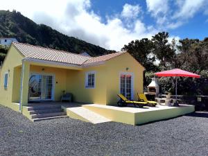 a small yellow house with two chairs and an umbrella at Houses of Eira Velha in Fajã do Ouvidor