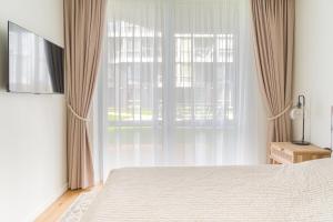 a bedroom with a bed and a large window at SimSim Apartamentai in Šventoji