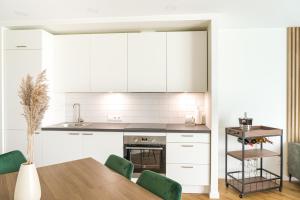 a kitchen with white cabinets and a table with green chairs at SimSim Apartamentai in Šventoji
