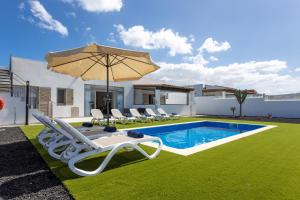 a pool with chairs and an umbrella next to a house at Luxury Villa Perla in Caleta De Fuste