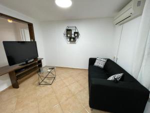 a living room with a black couch and a flat screen tv at אל מול חרמון- דירה באווירה כפרית עם נוף לחרמון in Sheʼar Yashuv +4 photos