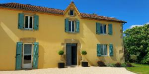 Una casa amarilla con persianas azules. en maison d'hôtes Le Courty, en Blousson-Sérian