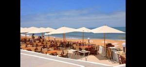 a beach with tables and chairs and white umbrellas at Appartement front de mer avec piscine en face des plages privées in Dar Bouazza