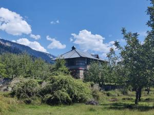 a building in the middle of a field with trees at Cliffer Cottage: Make Mountains Memorable! in Manāli