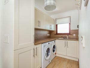 a kitchen with white cabinets and a washer and dryer at Craigievar in Cruden Bay