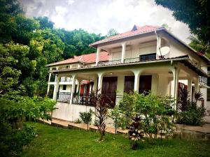 a large white house with a balcony and trees at La Canopée Enchantée, chambres d'hôtes, piscine, proche aéroport, Gare maritime in Les Abymes