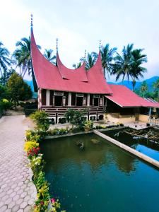 a house with a red roof next to a pond at Rumah Gadang Simarasok in Baso