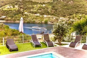 a pool with chairs and an umbrella and a boat in the water at Quintinha de Mirão - Douro Valley in Resende