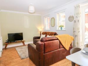 a living room with a brown leather couch and a television at Trinity Cottage in Christchurch
