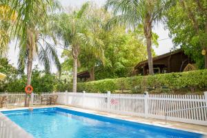 a swimming pool with a white fence and palm trees at Eden Ramot Chalets in Moshav Ramot