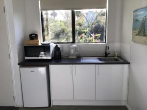 a kitchen with white cabinets and a microwave and a window at La Casita Waiheke in Oneroa