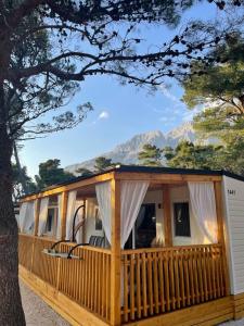 a wooden cabin with a large deck with mountains in the background at Mobile Homes Dololego - Camp Baško Polje in Baška Voda