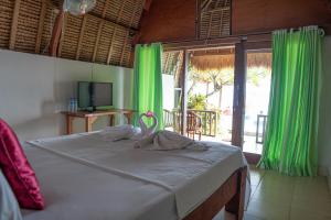 a bedroom with a bed with green curtains and a television at Krisna Bungalows and Restaurant in Sekotong