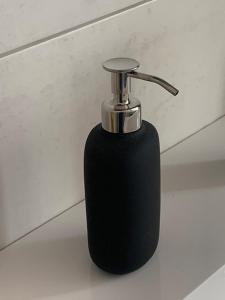 a black soap dispenser sitting on top of a wall at New Home Guest House in Gödöllő