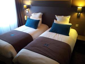 two beds in a hotel room with blue pillows at Moka Hotel in Niort