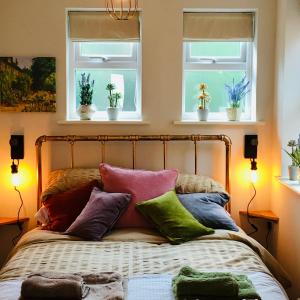 1 cama con almohadas coloridas y 2 ventanas en The Art Attic a Stylish Boutique Apartment en Builth Wells