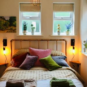 a bed with colorful pillows on it with two windows at The Art Attic a Stylish Boutique Apartment in Builth Wells