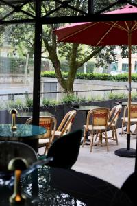 eine Terrasse mit Stühlen, Tischen und einem Sonnenschirm in der Unterkunft Hôtel De Charme Le Chêne Vert in Brive-la-Gaillarde