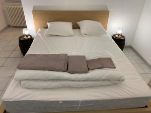 1 cama grande con sábanas blancas y almohadas marrones en Gîte le cœur de Givry, en Givry