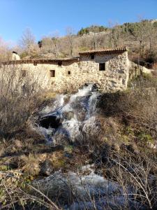 a stone building next to a river in a field at Las Tejeruelas Casa Rural in Navacepedilla de Corneja