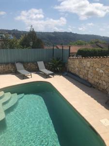 een zwembad met 2 stoelen en een stenen muur bij appartement en rez de villa in Gattières