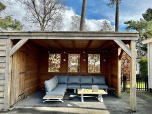 a wooden pavilion with a couch and a table at Chalet Bosrand 42 Park Veluwshof 6 p in Hoenderloo