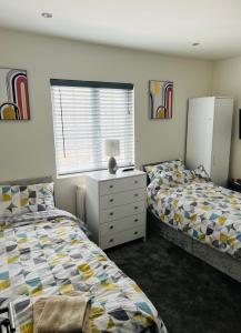 a bedroom with two beds and a dresser and a window at Green Lantern, Private En-suite Double Bedroom in Aveley