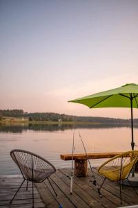 dos sillas y una sombrilla en un muelle junto a un lago en Niezwykła Cisza Glamping & Sauna, en Zelwa