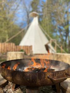 a grill with fire in it with a white pyramid in the background at Glamping Nad Meandry in Unhošť