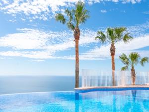 a swimming pool with palm trees and the ocean at Apartment Azul Celeste by Interhome in Benitachell