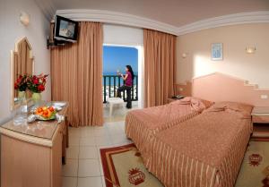 una habitación de hotel con una cama y una mujer mirando por la ventana en Hotel Royal Beach, en Sousse