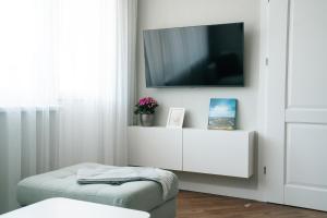 a white living room with a tv and a ottoman at Grey Green Cozy Apartment in Birštonas