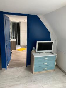 um quarto com uma televisão numa cómoda e uma parede azul em Le Mesnil Normand em Fort-Moville
