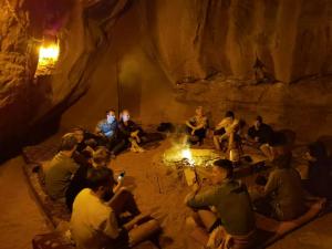 a group of people sitting around a fire in a cave at desert colored camp in Wadi Rum