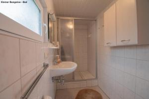 a white bathroom with a sink and a shower at Kleiner Bungalow - Zum Strand 50m in Ueckeritz