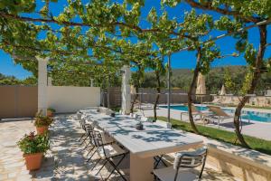 a long white table and chairs on a patio with a pool at Villa Pergola in Pandokrátor