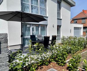 a patio with a table and chairs and an umbrella at Lee-Moderne Neubauwohnung in Strandnähe - Wallbox in Wremen