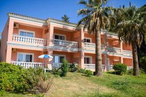 a large orange building with a balcony and palm trees at Paleo Apartments in Paleokastritsa