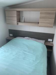 a bedroom with a bed with blue sheets and wooden cabinets at CLJP Caravan Thorpe Park Cleethorpes Free WI-FI in Cleethorpes