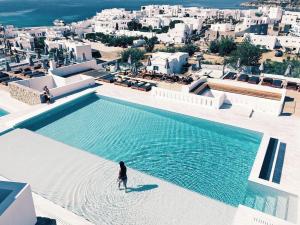 una persona de pie junto a una gran piscina de agua en The George Hotel Mykonos, en Platis Gialos