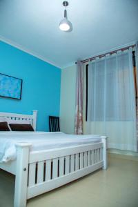 a blue bedroom with a white bed and a window at Keisha Luxury Furnished Apartment Bukoto in Kampala