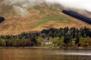 a house on the shore of a lake in front of a mountain at Butlers Quarters Apartment in Cairndow