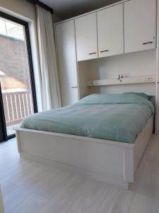 a white bedroom with a bed with a large window at Casa Quatre-Mains Westende in Westende