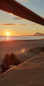 un tramonto su una spiaggia con l'oceano e una panchina di XimoApartments AP-3 Primera LÍNEA Playa y CHIMENEA a Oliva
