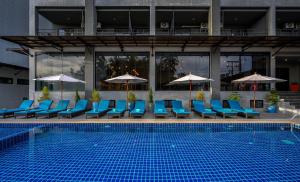 una piscina con sillas azules y sombrillas junto a un edificio en Maikhao Hotel managed by Centara - SHA Extra Plus, en Mai Khao Beach