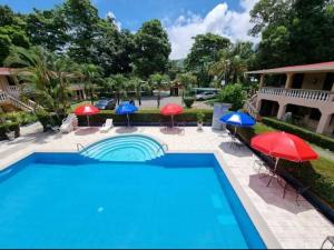a swimming pool with red and blue umbrellas and chairs at House of the Macaws in Tarcoles