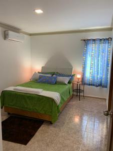 een slaapkamer met een bed met een groene deken en blauwe gordijnen bij Stylish 2R-2B Apt Near the Beach and Main Street in Sosúa